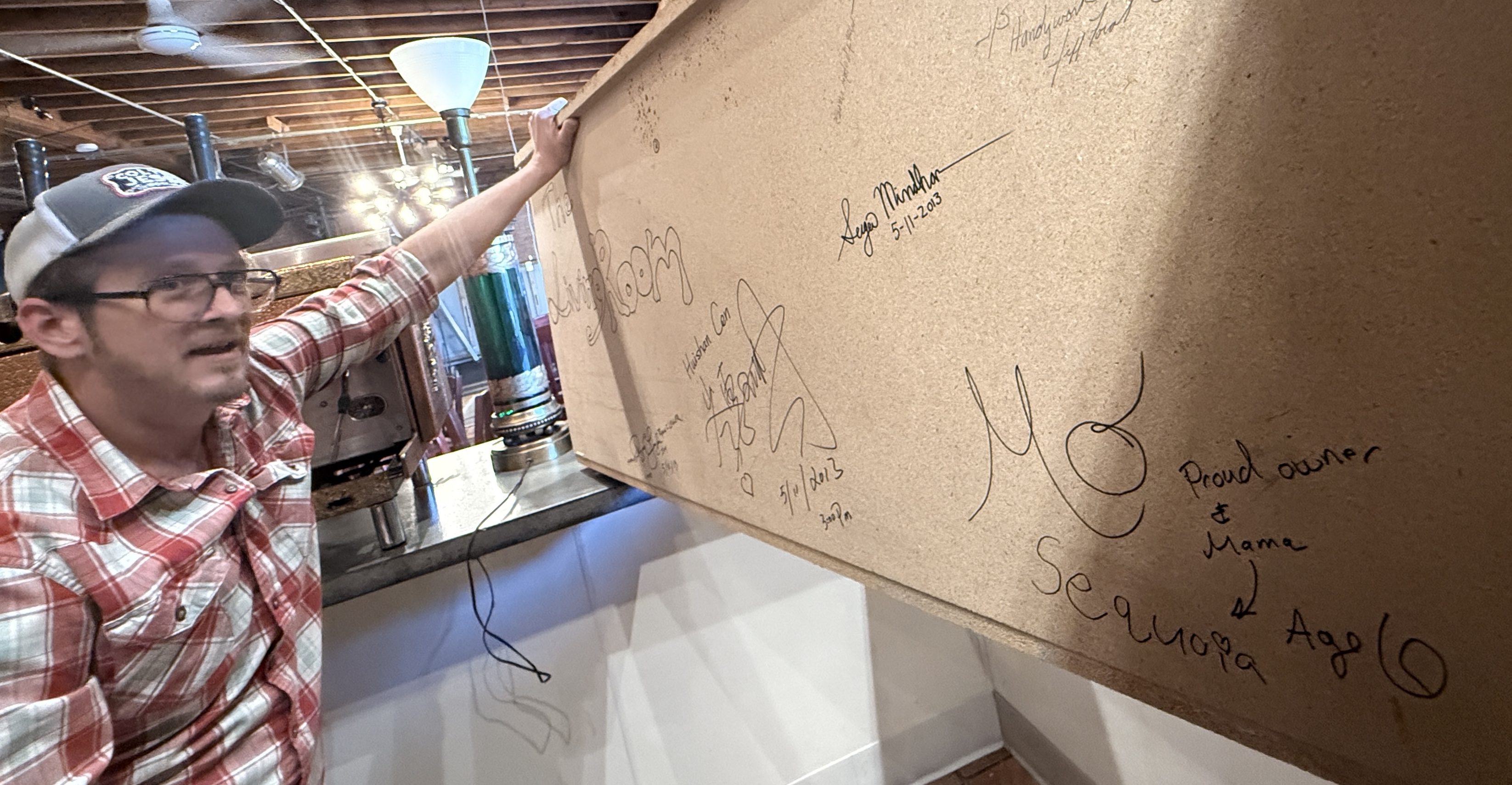Pencil signatures on raw plywood under a half-built bar in Sheridan, late at night